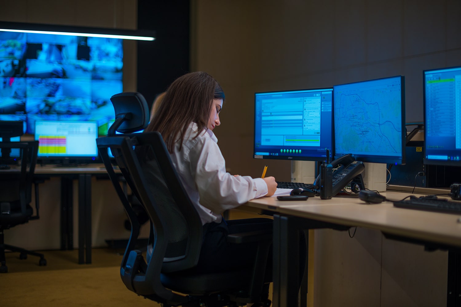 Female security guard sitting and monitoring modern CCTV cameras in a surveillance room.